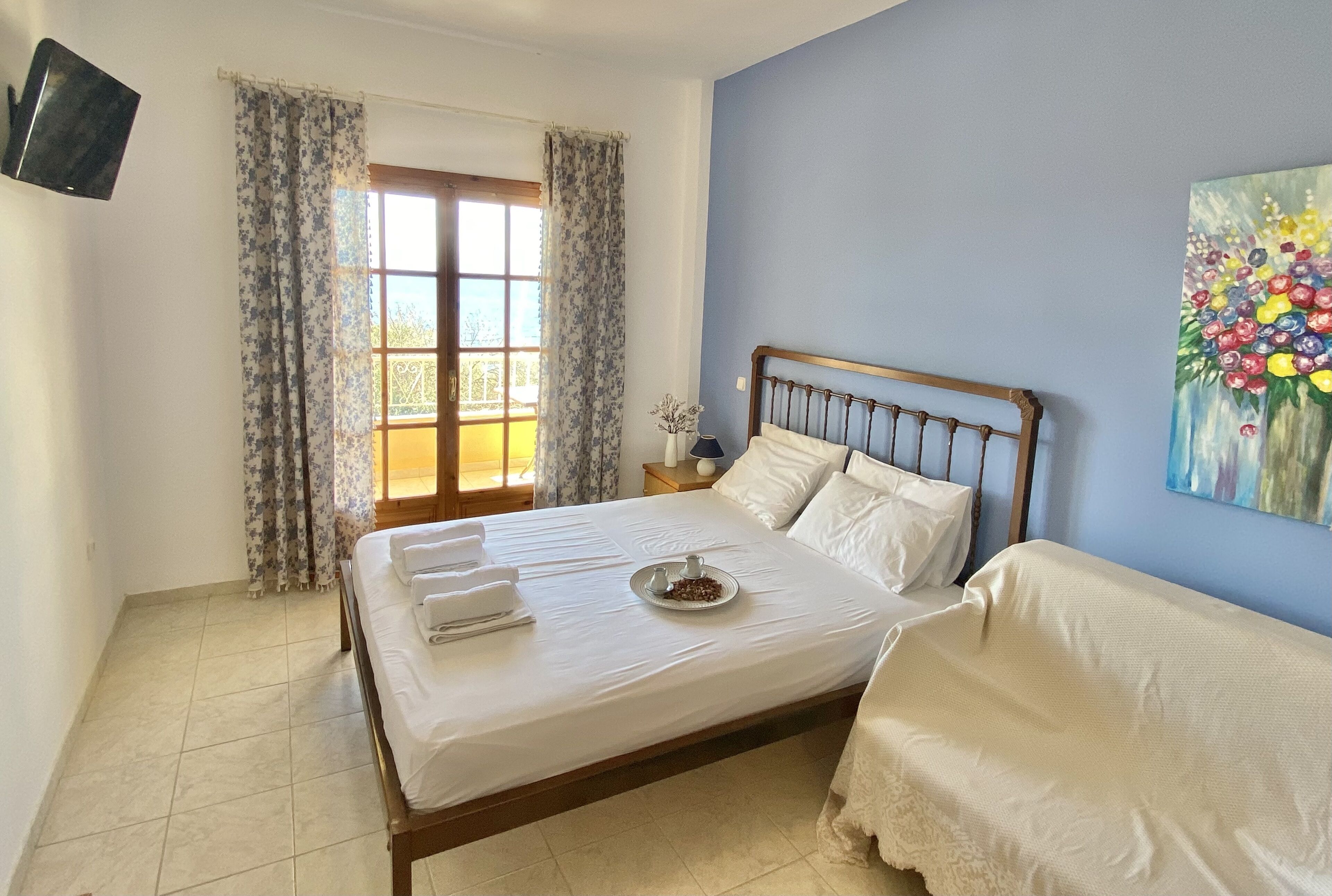 Una cama bien hecha con sábanas blancas y una bandeja de comida, una mesita de noche con una lámpara y un cuadro en la pared.