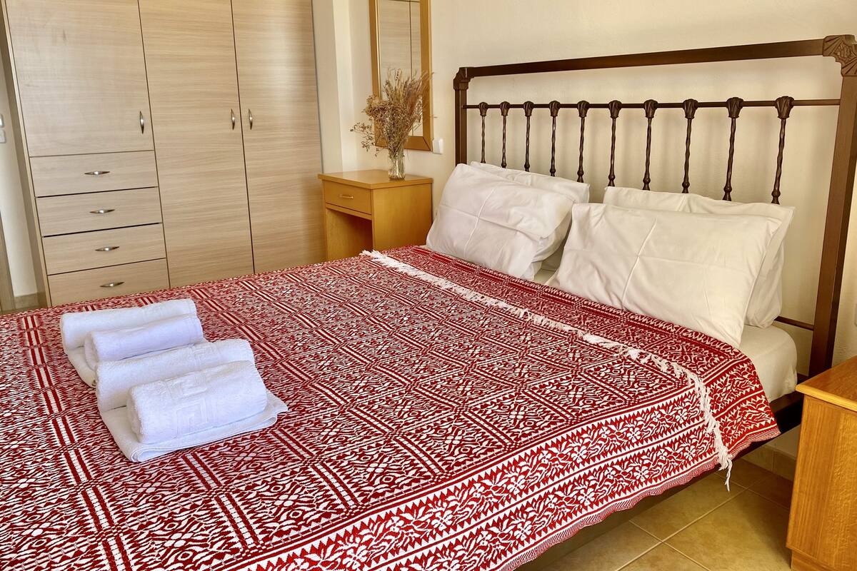 A neatly made bed with a patterned bedspread, a wooden headboard, and white pillows.