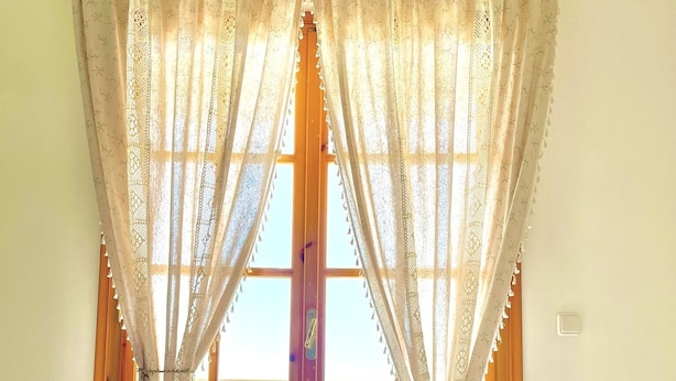 A breakfast tray with orange juice, croissants, and a bowl of fruit on a bed with a view of the sea through sheer curtains. - Armonia - Elegant Apartments (Mantoudi-Limni-Agia Anna)