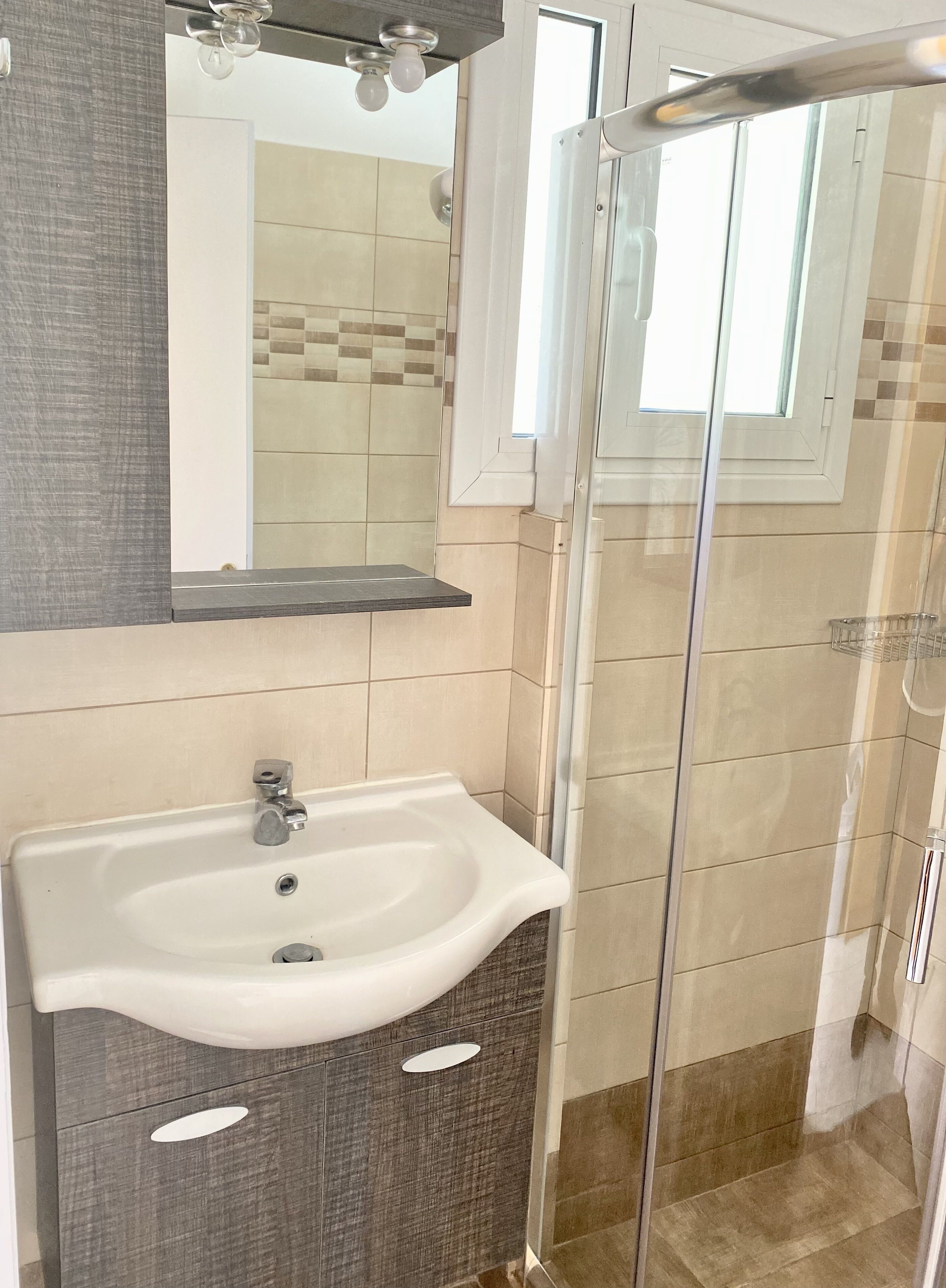 Un baño con lavamanos blanco, un espejo y zona de ducha.