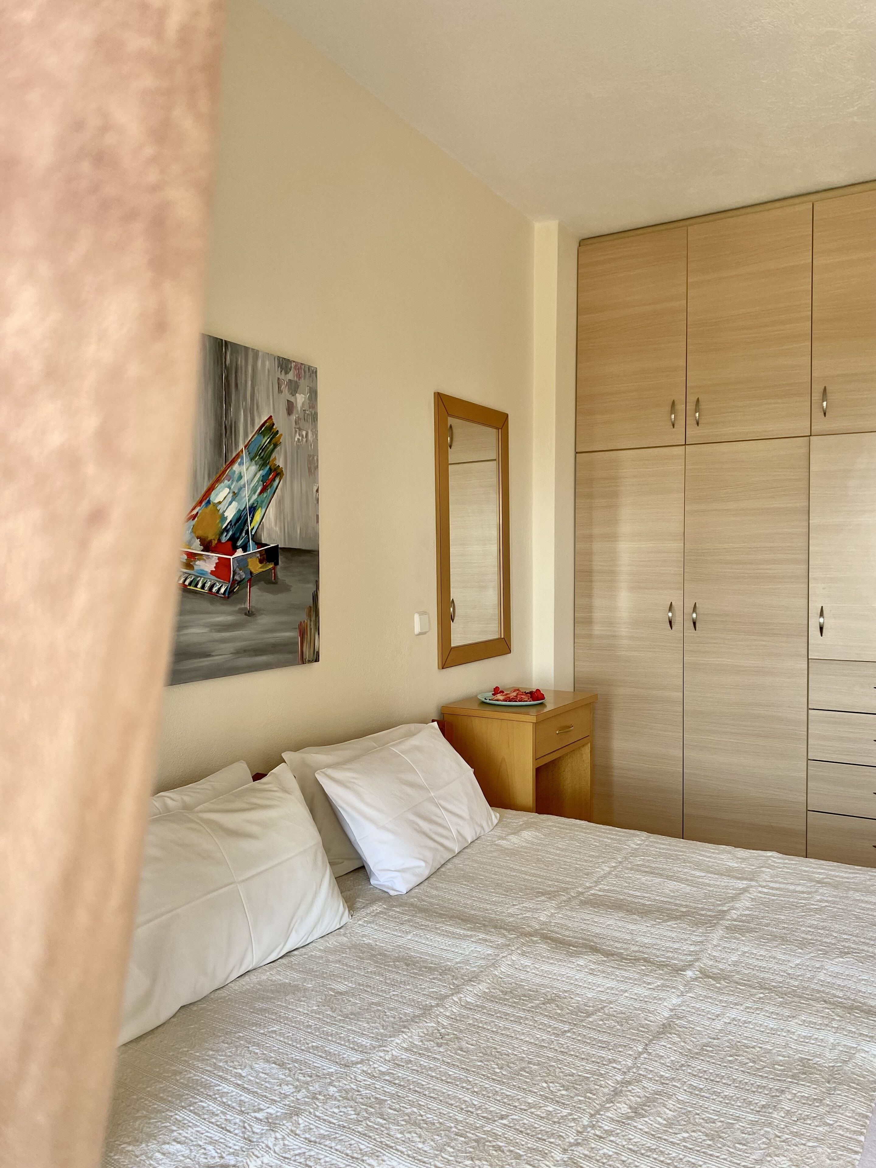 Een slaapkamer met een bed, een houten garderobe, een klein tafeltje met fruit en een schilderij aan de muur.