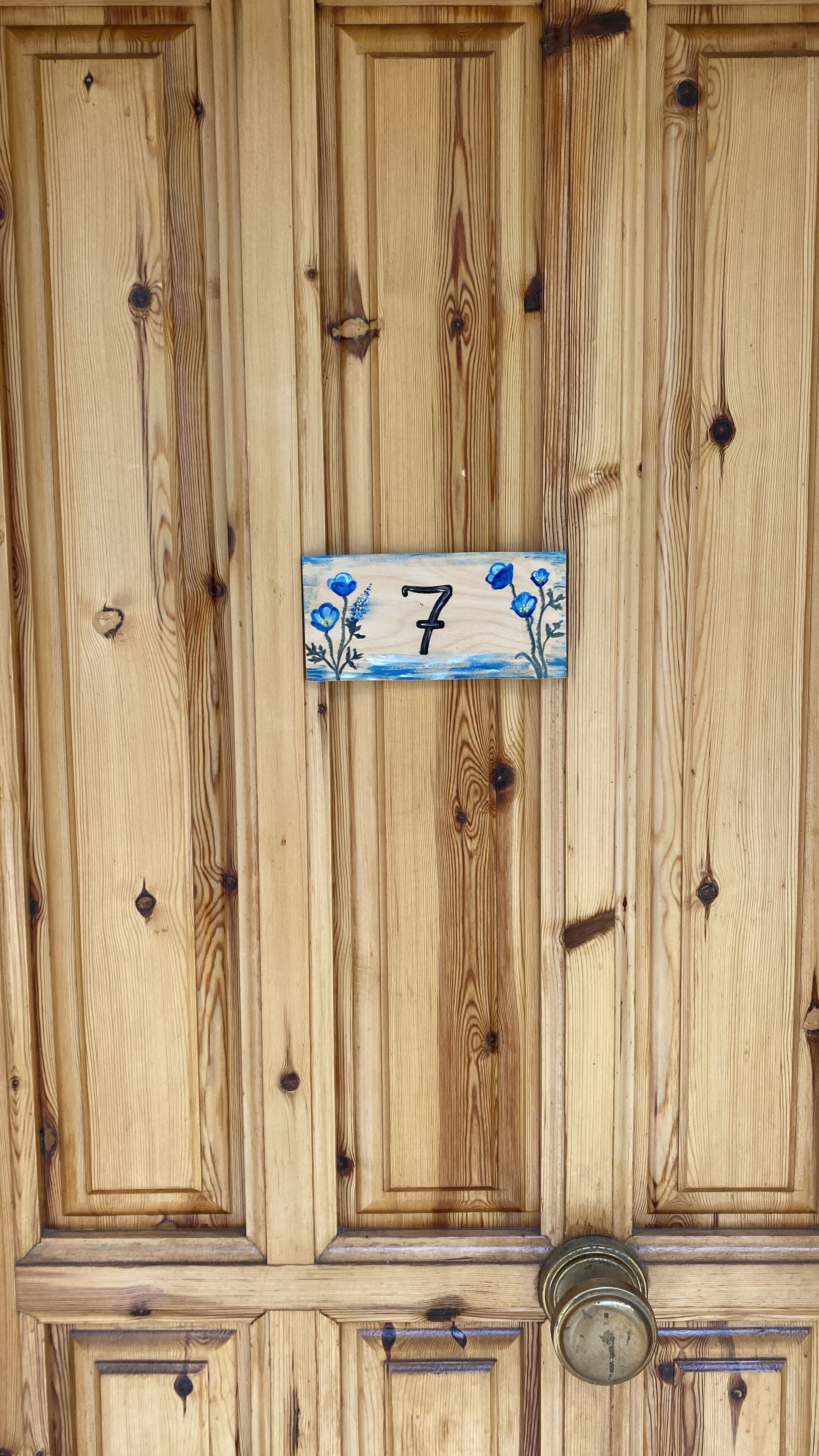Una porta in legno con una targa con il numero '7' e un bussolotto di ottone.