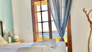 A hotel room with a large bed, a window with curtains, a vase with flowers, and a wooden tree sculpture. - Armonia - Elegant Apartments (Mantoudi-Limni-Agia Anna)