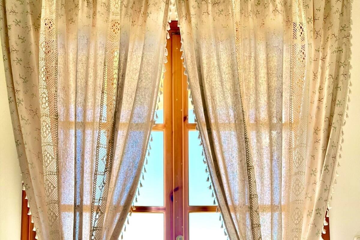A breakfast tray with pastries, a glass of orange juice, and a cup of coffee on a table by a window with lace curtains.