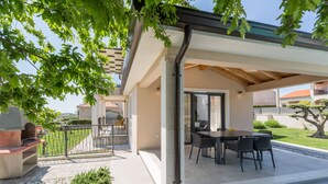 An outdoor patio with a dining table and chairs, a barbecue grill, and a pergola structure. - Villa for 4-6 people, pool, loungers, garden, panoramic sea view (Poreč)