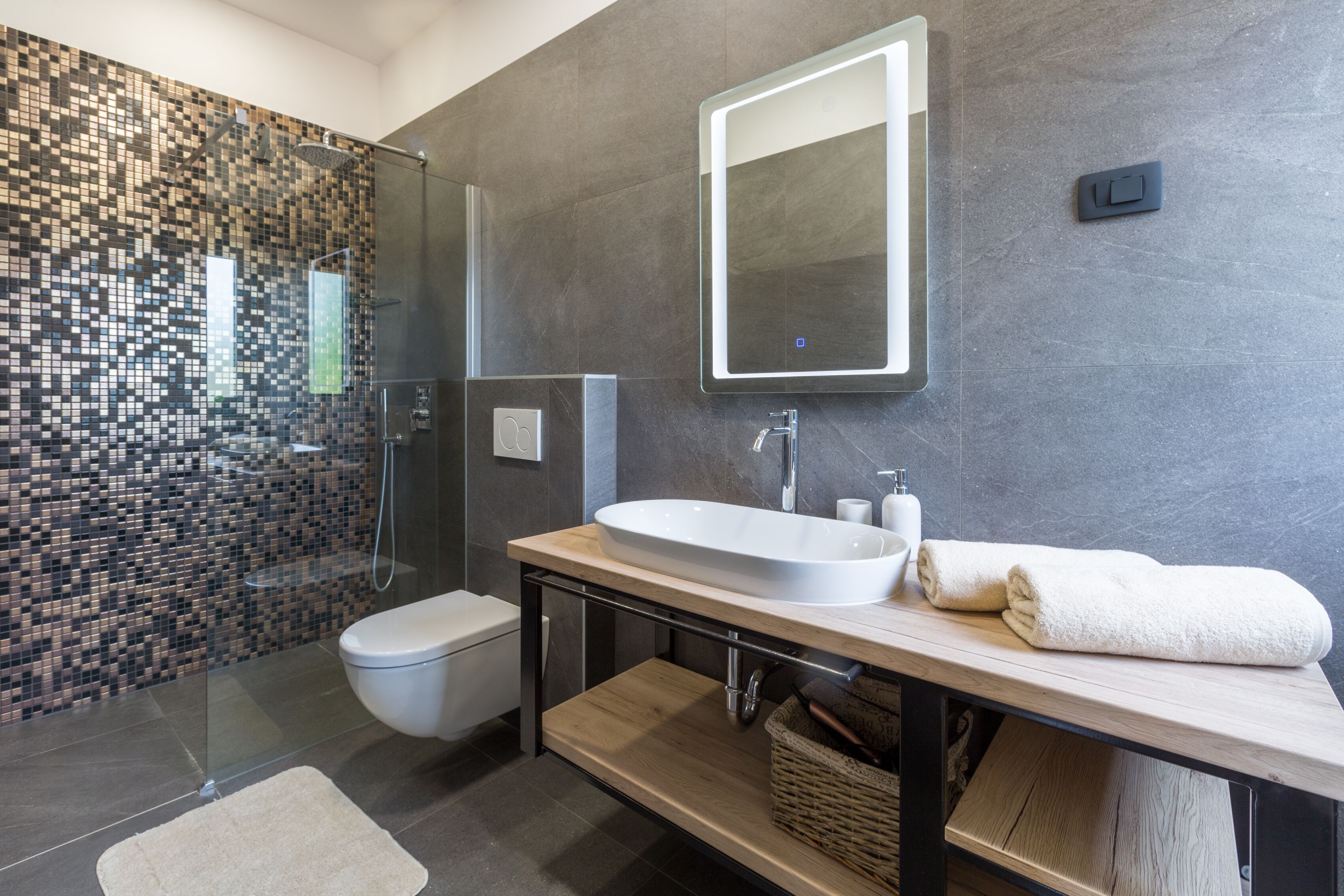 A modern bathroom with a glass shower enclosure, a toilet, a sink with a mirror, and a towel on the counter.