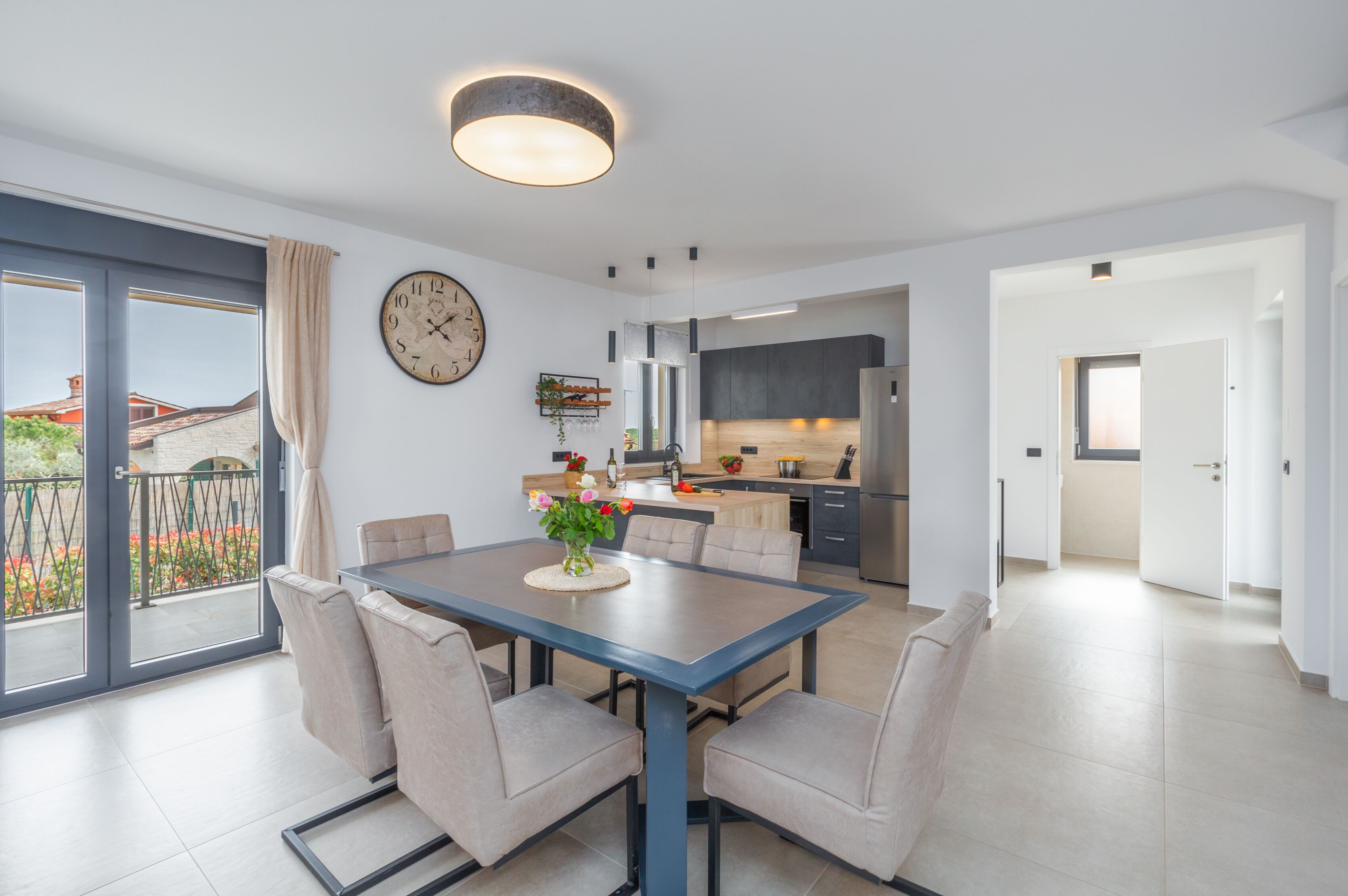A modern apartment with a dining area, kitchen, and a balcony with a view of buildings.