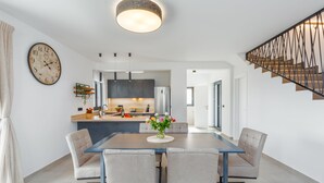 A modern kitchen with a central island, a dining area with a glass table and chairs, and a staircase with a metal railing. - Villa for 4-6 people, pool, loungers, garden, panoramic sea view (Poreč)