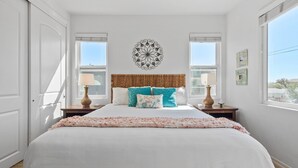 A bedroom with a large bed, two bedside tables, a decorative wall piece, and a window with blinds.