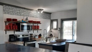 A modern kitchen with a stainless steel range, a built-in oven, and a microwave. There are red mugs on a shelf, a coffee maker, and a sink with a faucet. A framed sign with an anchor logo is on the counter.