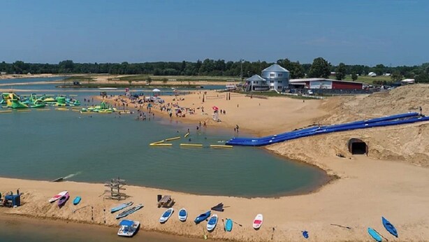 A beach with a water slide, boats, and a sandy area with umbrellas.