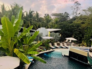 A pool area with lounge chairs and umbrellas, surrounded by lush greenery and a waterfall feature. - 10 bedroom estate - walk to beach salt water pool (playa potrero)