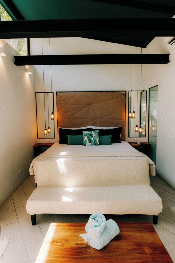 A modern bedroom with a large bed, bedside tables, and a bench. - 10 bedroom estate - walk to beach salt water pool (playa potrero)