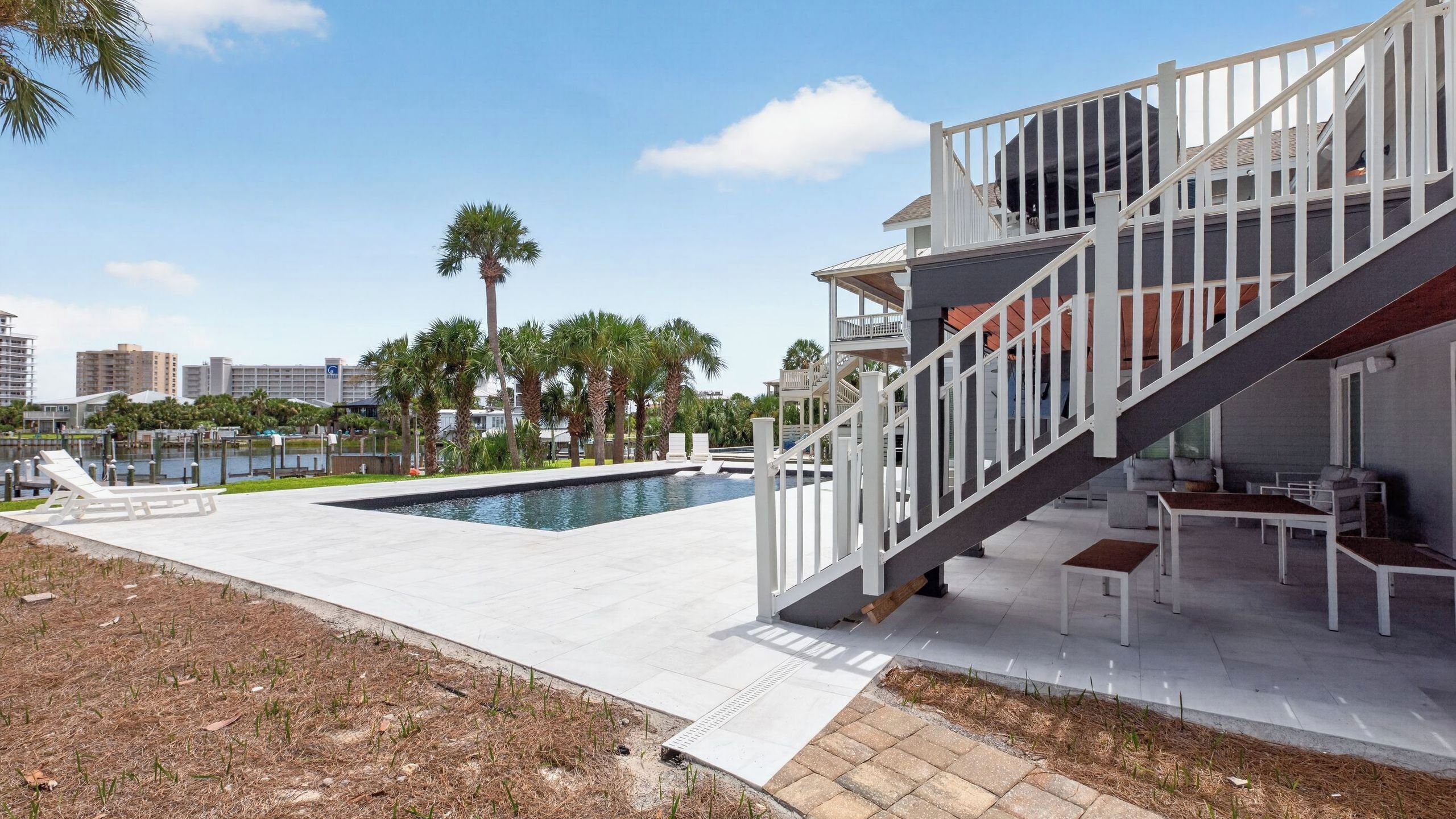 Zona moderna de piscina al aire libre con una escalera que lleva a un balcón, rodeada de palmeras y vistas al horizonte de la ciudad.