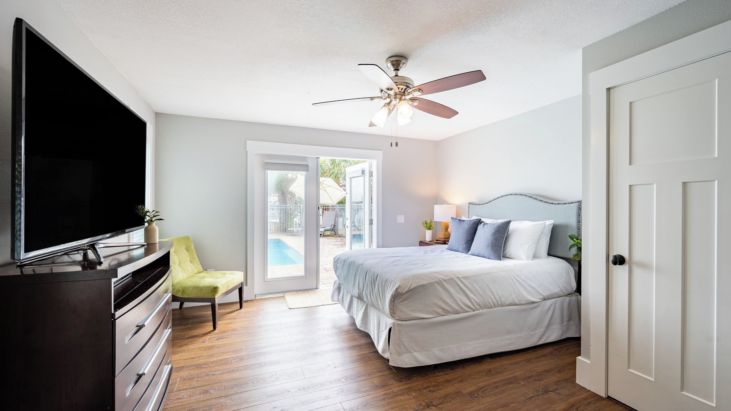 A bedroom with a bed, a TV, a chair, and a ceiling fan.