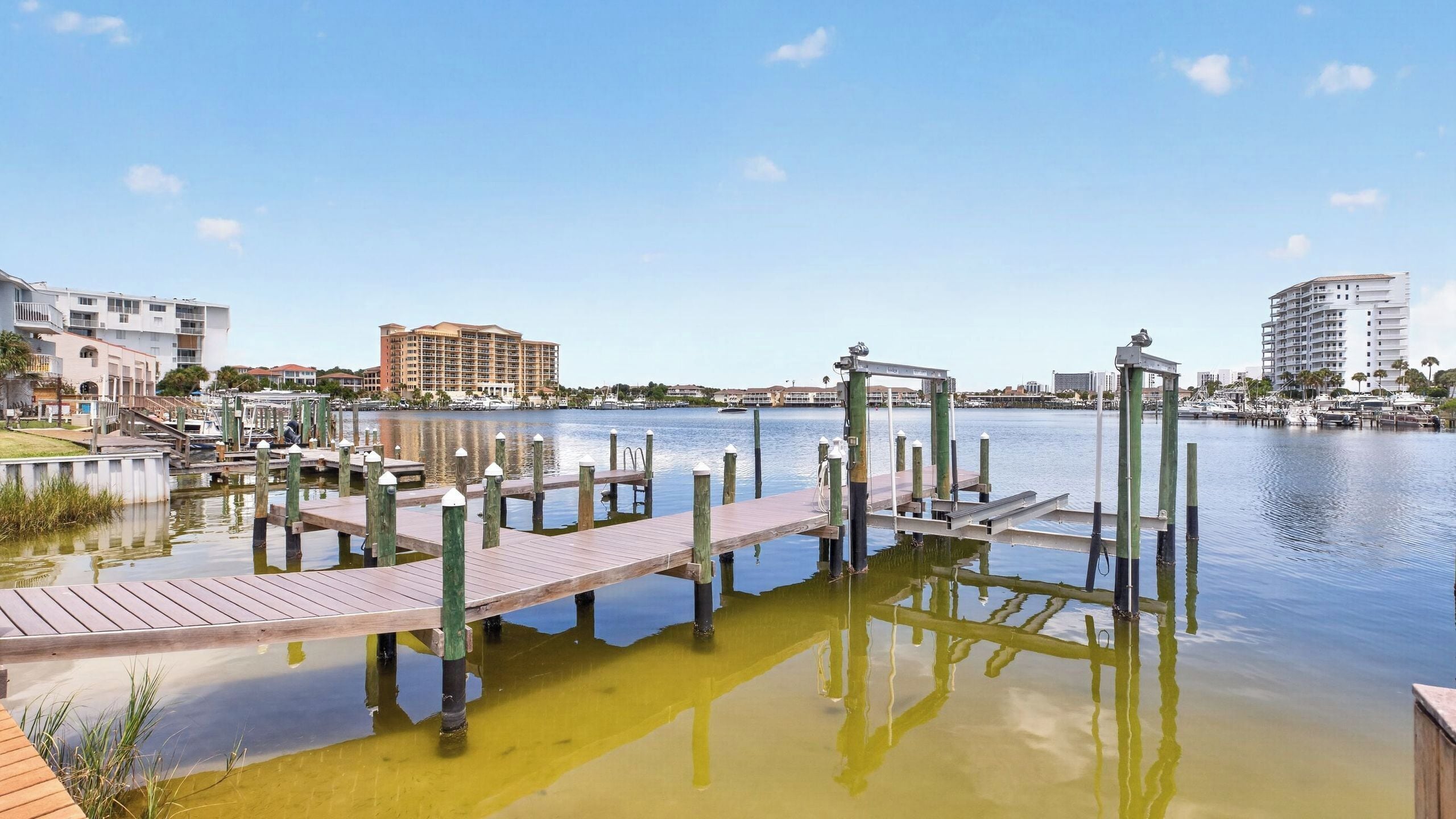 A marina with wooden docks and boats, surrounded by buildings and a clear sky.