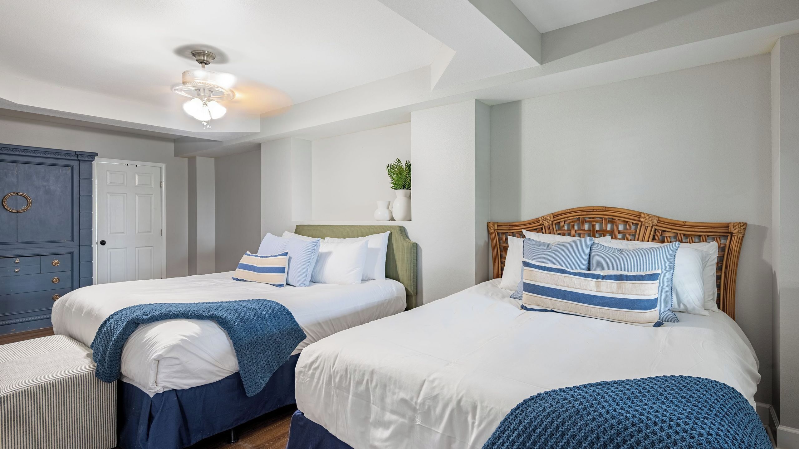Habitación de hotel con dos camas, un ventilador de techo, un armario y una planta pequeña.