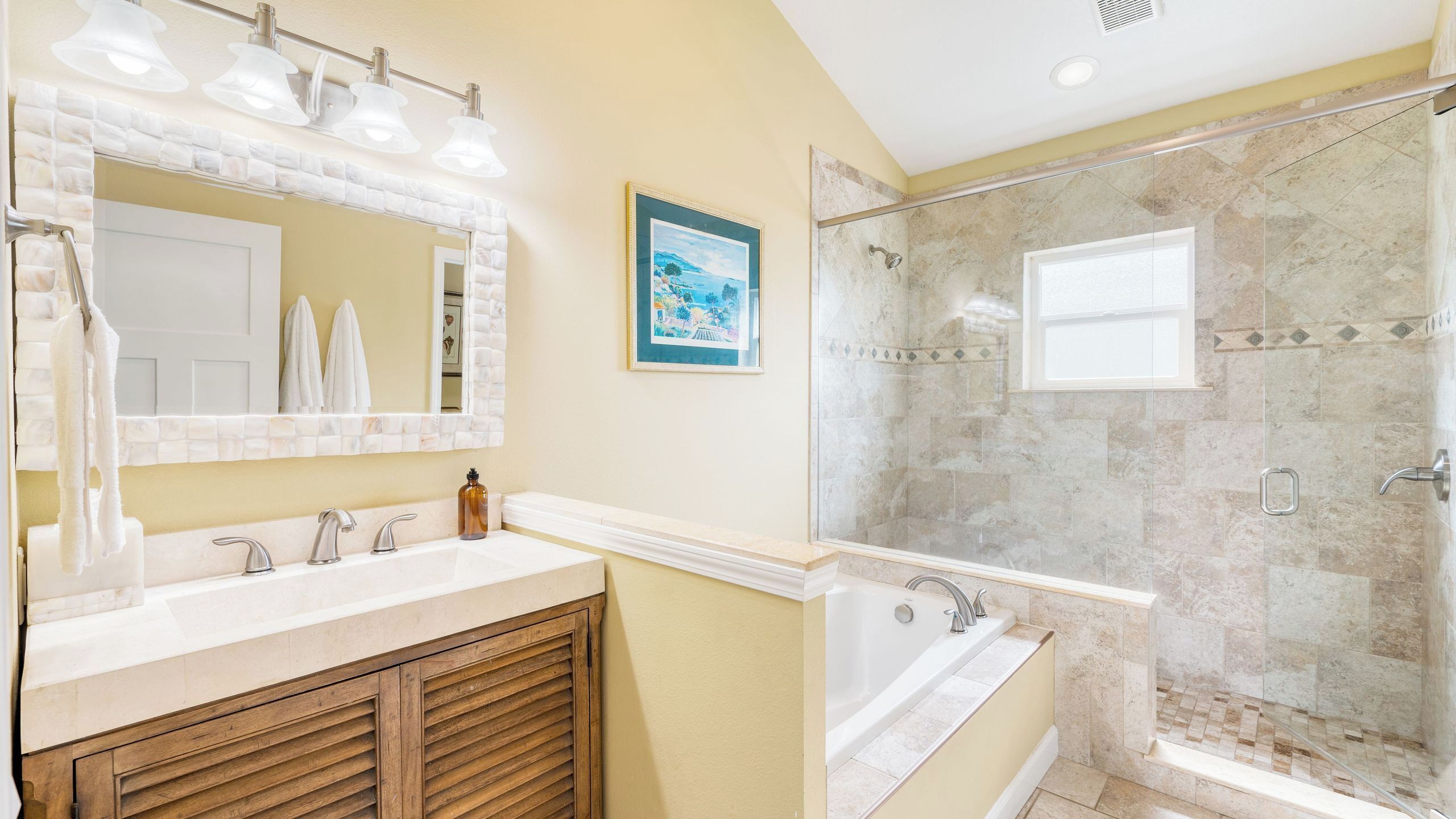 A bathroom with a double vanity, a bathtub, a shower with a glass door, and a framed picture on the wall.