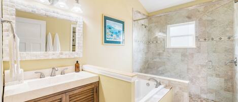 A bathroom with a double vanity, a bathtub, a shower with a glass door, and a framed picture on the wall.