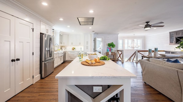 A modern kitchen with white cabinetry, a large island, and a dining area with a wooden table and beige sofa.