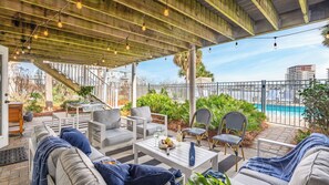 A covered outdoor patio with seating, a pool, and a view of the city.