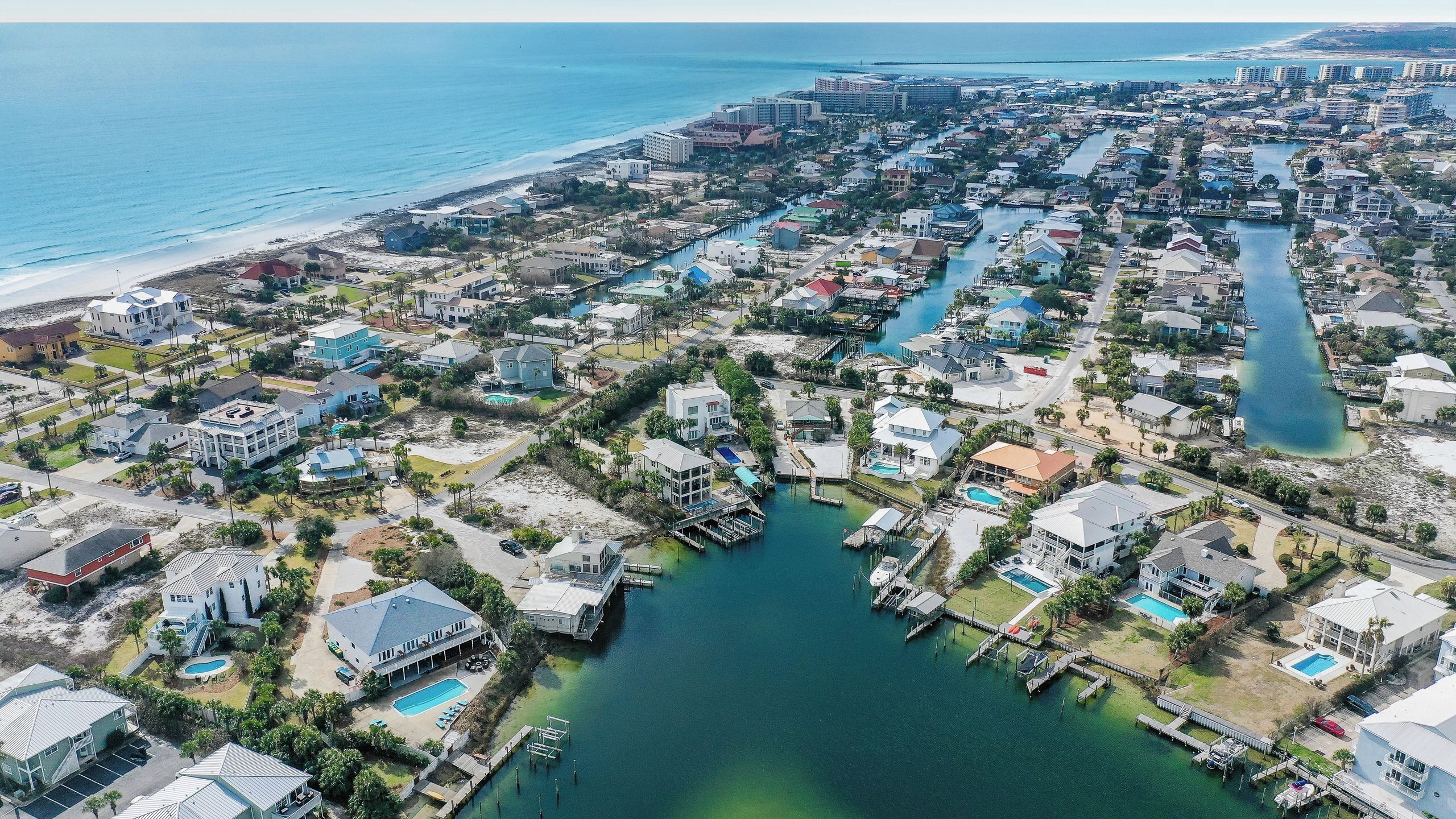 An aerial view of a coastal residential area with houses, a marina, and a beach.