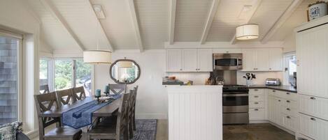 Una cocina con muebles blancos, una isla central y un comedor con sillas y una mesa de madera.