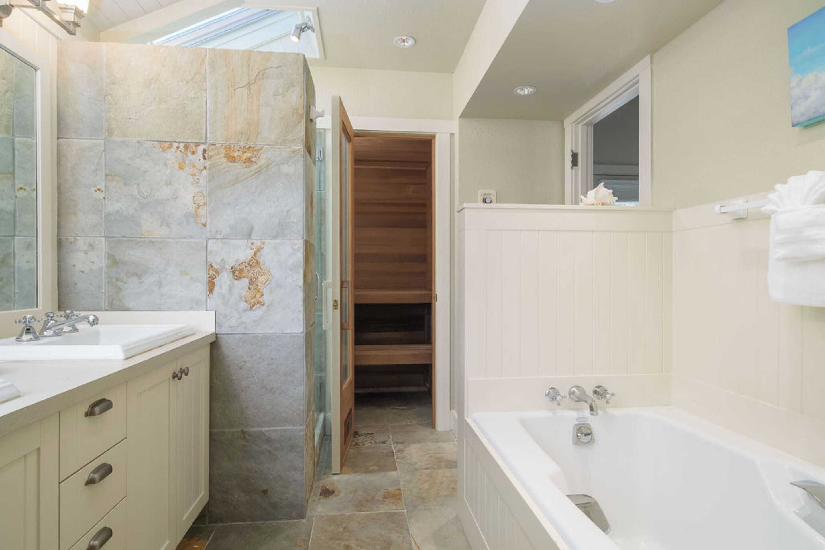 Une salle de bain avec un mur en marbre, une baignoire et une porte en bois donnant sur un placard.