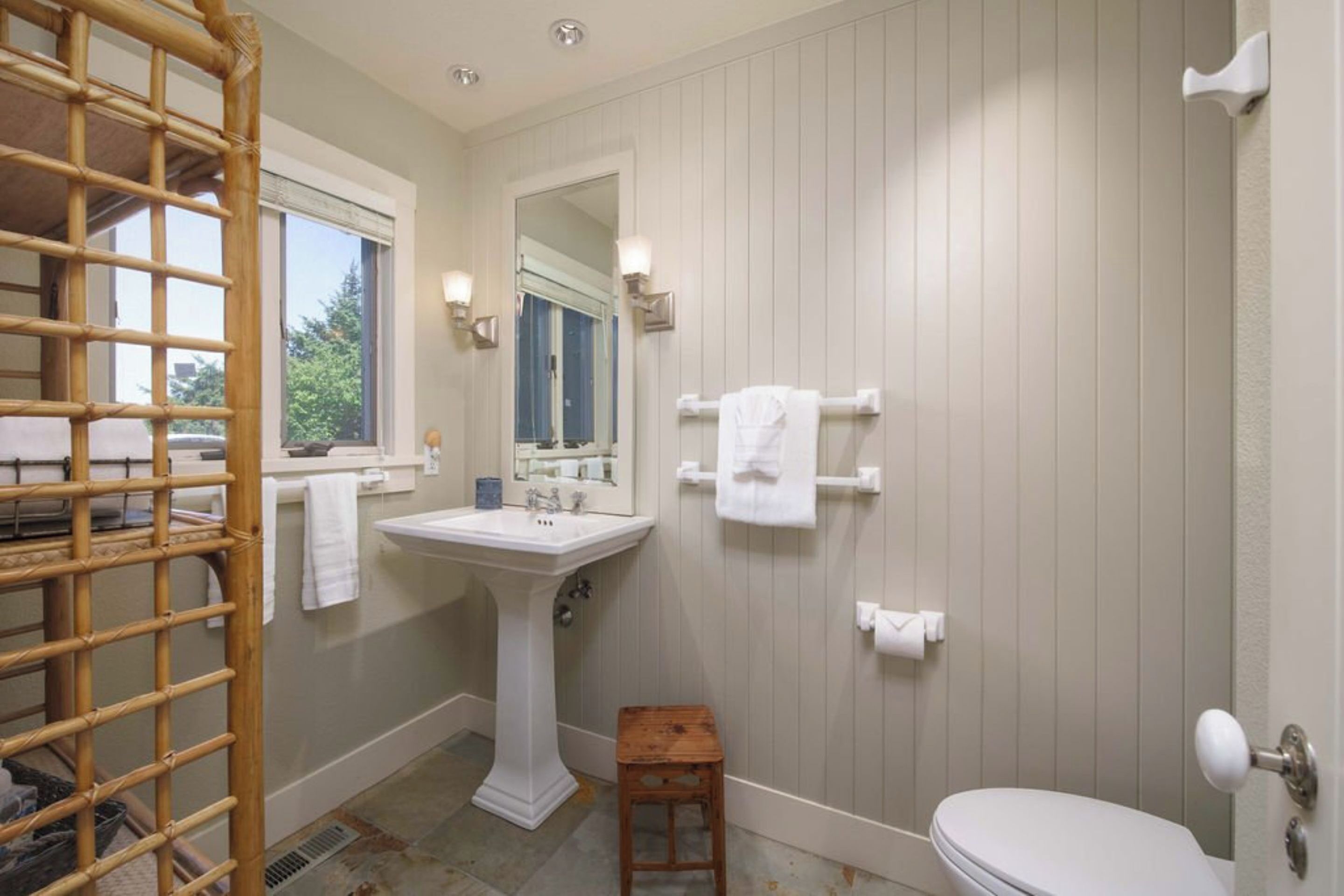 A bathroom with a white sink, mirror, and toilet, wooden floor, and a window with a view.