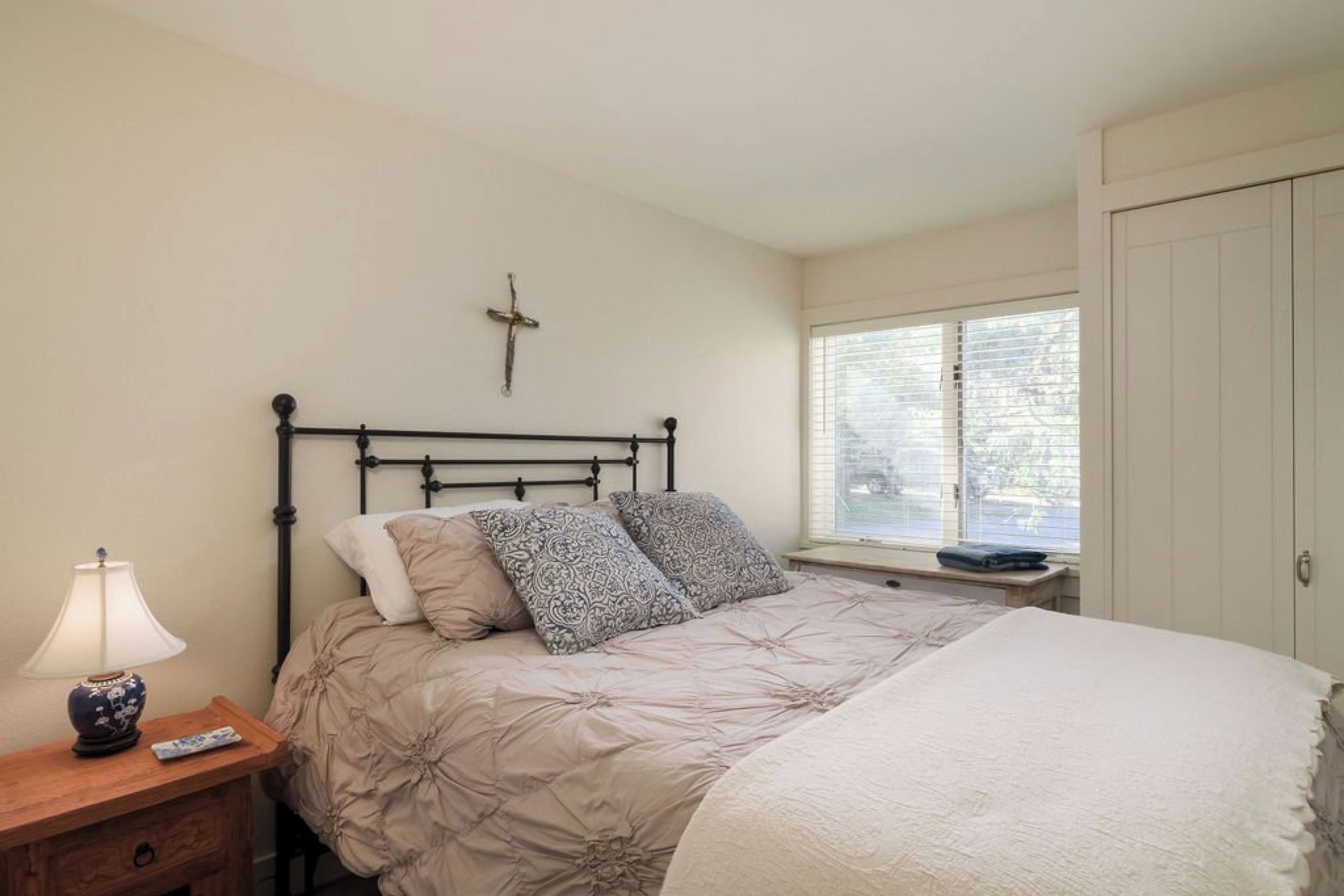 A bedroom with a bed, bedside table, lamp, and a window with blinds.