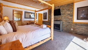 A bedroom with a four-poster bed, a stone fireplace, and a ceiling fan.