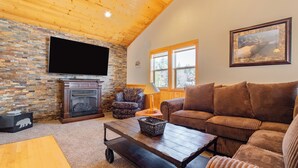 A cozy living room with a stone fireplace, a television, a large window, and a brown couch.