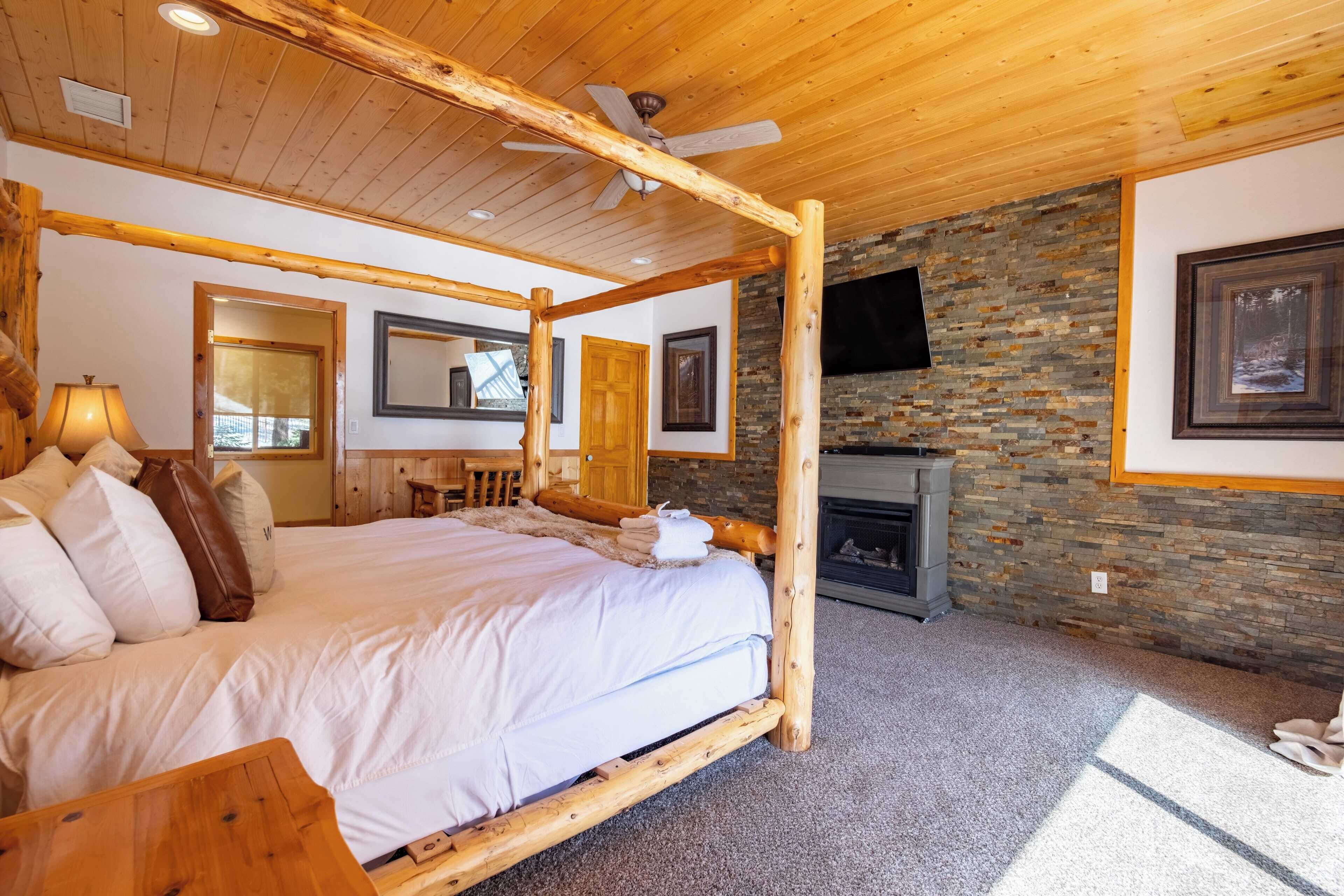 A bedroom with a four-poster bed, a stone fireplace, and a ceiling fan.