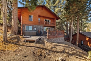 Une cabane en rondins à deux étages, avec des fondations en pierre, un balcon et un jacuzzi.