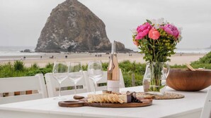 A table set with wine glasses, a bottle of wine, cheese, flowers, and a wooden bowl on a beach view. - Oceanfront w/ Direct Beach Access Game Room Views Driftaway by Avantstay (Cannon Beach)