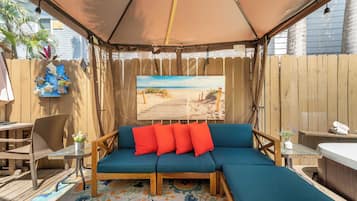Relax in this serene outdoor seating area with a comfortable sofa, a small table, and a chair, surrounded by lush greenery and a beautiful beach scene.