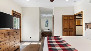 A bedroom with a bed, a dresser, a television, and a bathroom visible through an open door. - Walk to Lake 6BR Cabin w/ Game Room, Hot Tub Big Bear Castle (Big Bear Lake)