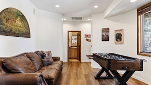 A room with a leather sofa, a foosball table, and a painting on the wall. - Walk to Lake 6BR Cabin w/ Game Room, Hot Tub Big Bear Castle (Big Bear Lake)