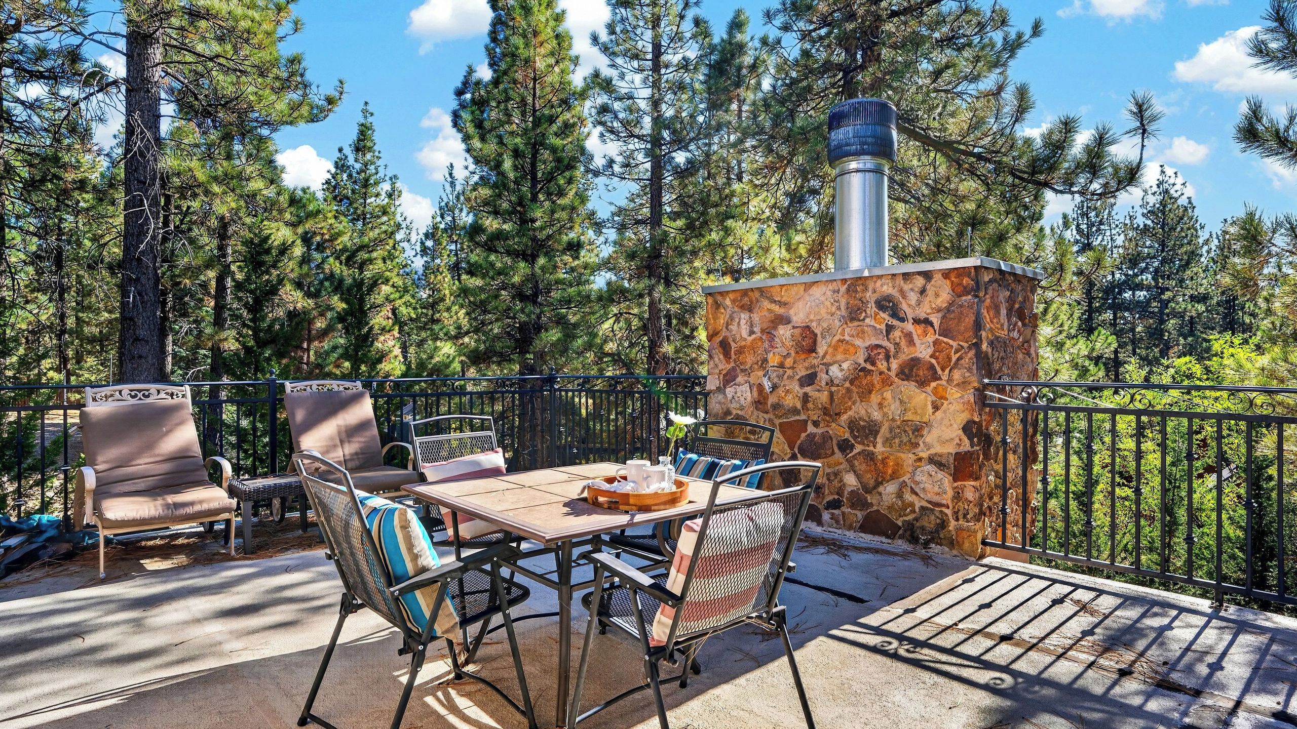 An outdoor patio with a stone wall, metal railing, and a table with chairs.