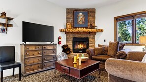 A living room with a fireplace, a television, a sofa, and a coffee table. - Walk to Lake 6BR Cabin w/ Game Room, Hot Tub Big Bear Castle (Big Bear Lake)