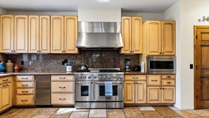 A kitchen with wooden cabinets, stainless steel appliances, and a granite countertop. - Walk to Lake 6BR Cabin w/ Game Room, Hot Tub Big Bear Castle (Big Bear Lake)