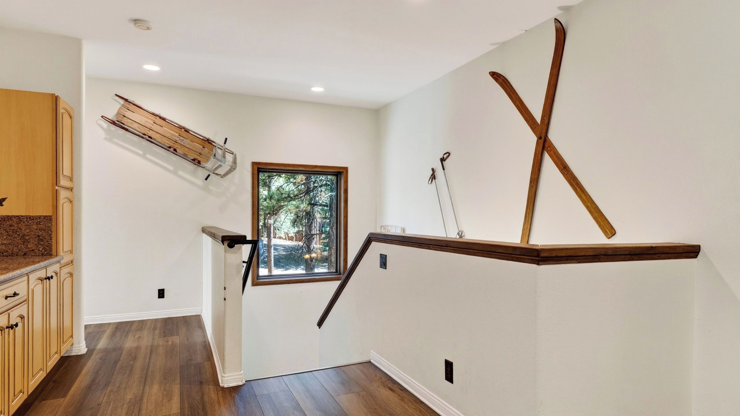 A staircase with wooden handrails, a window with a view of trees, and a wooden shelf with skis.