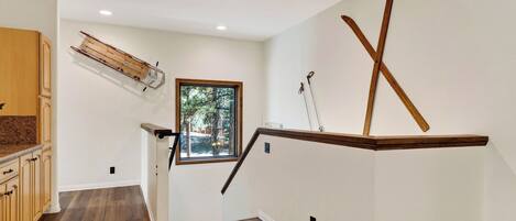 A staircase with wooden handrails, a window with a view of trees, and a wooden shelf with skis.