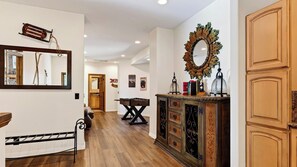 A hallway with a wooden floor, a dining table, and a cabinet with decorative items. - Walk to Lake 6BR Cabin w/ Game Room, Hot Tub Big Bear Castle (Big Bear Lake)