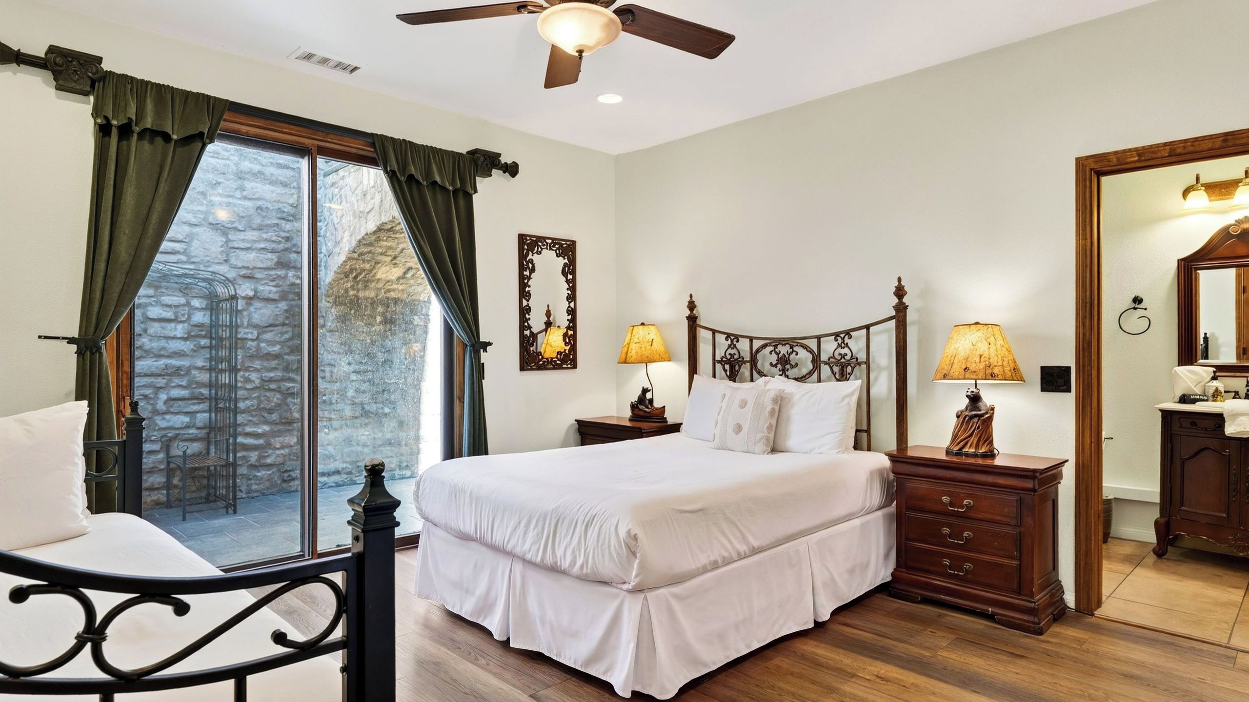 Une chambre à coucher avec un lit, des tables de chevet, une commode, un miroir et une vue sur l’extérieur par une fenêtre.