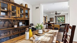 A dining area with a wooden table, chairs, a buffet cabinet, and a view of the outdoors through a window. - Walk to Lake 6BR Cabin w/ Game Room, Hot Tub Big Bear Castle (Big Bear Lake)