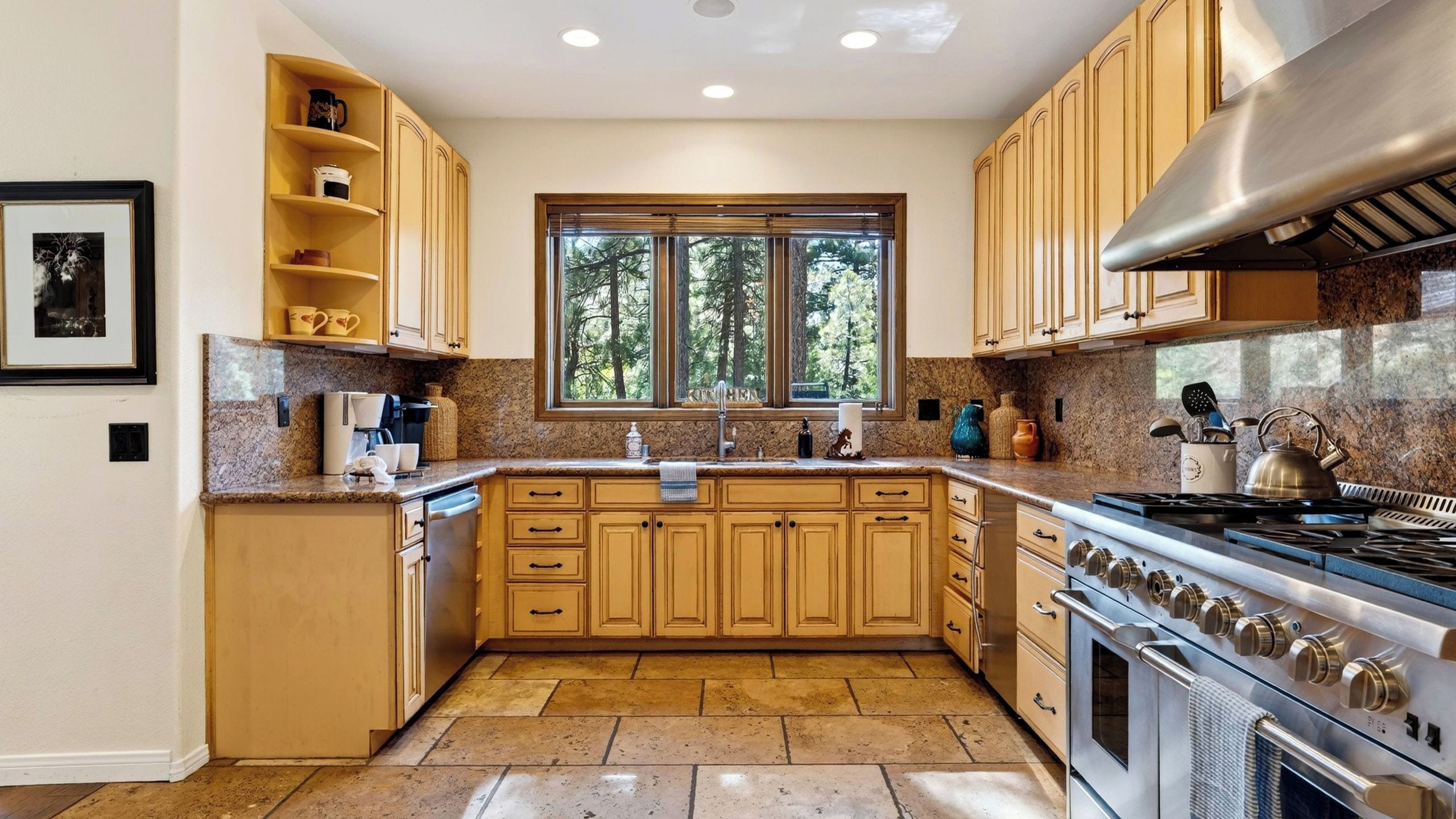 Una cocina con armarios de madera, una estufa de acero inoxidable y una ventana con vistas a árboles.