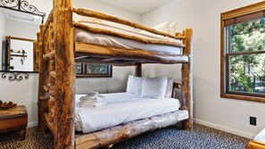 A bunk bed with a rustic wooden frame, white bedding, and a window with a view of trees. - Walk to Lake 6BR Cabin w/ Game Room, Hot Tub Big Bear Castle (Big Bear Lake)