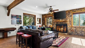 A living room with a stone fireplace, leather sofa, and a pool table. - Walk to Lake 6BR Cabin w/ Game Room, Hot Tub Big Bear Castle (Big Bear Lake)