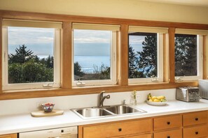 Eine Küche mit einem großen Fenster mit Blick auf ein Gewässer, einem Spülbecken, einem Toaster und einer Schüssel mit Obst.